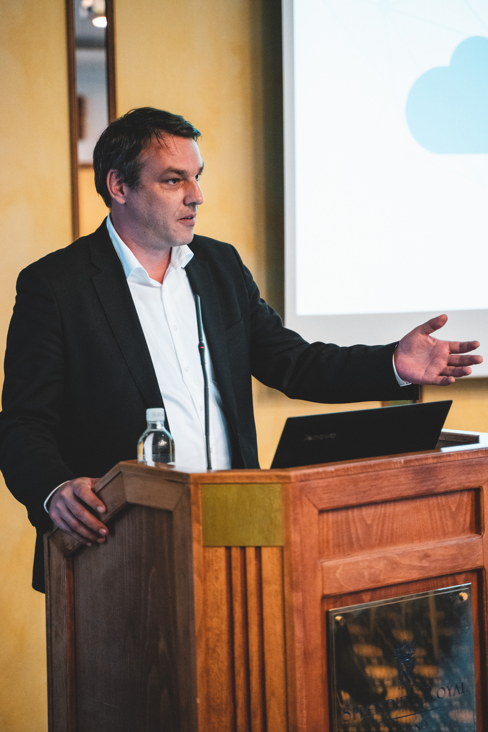 Gregor Zebic presenting from a wooden podium with a cloud-computing slide projected behind him