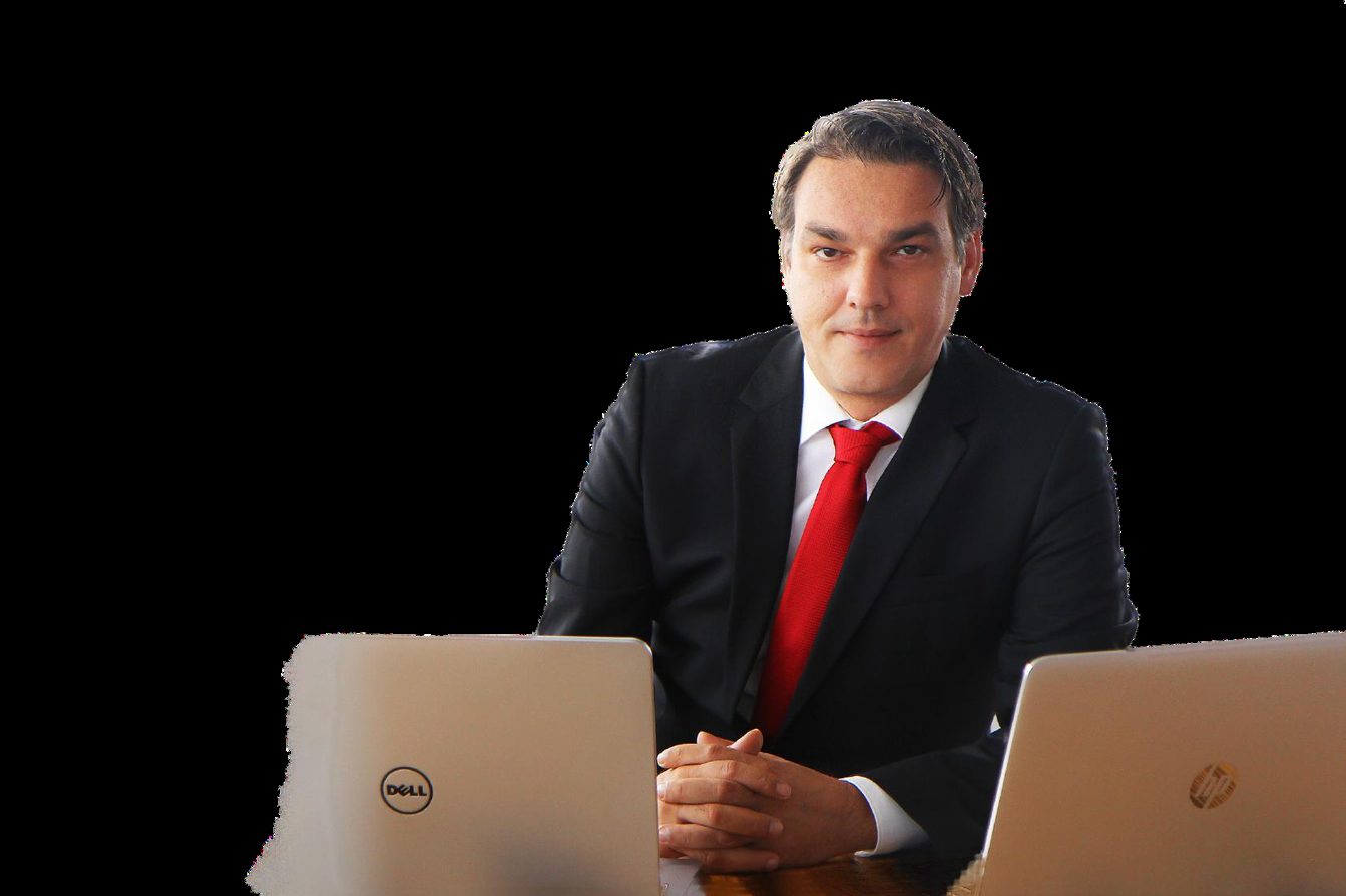 Gregor Zebic at his desk between two open laptops, wearing a dark suit and red tie